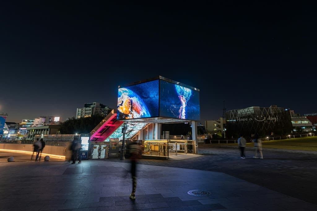 Structură cu ecrane LED într-o piață urbană, noaptea