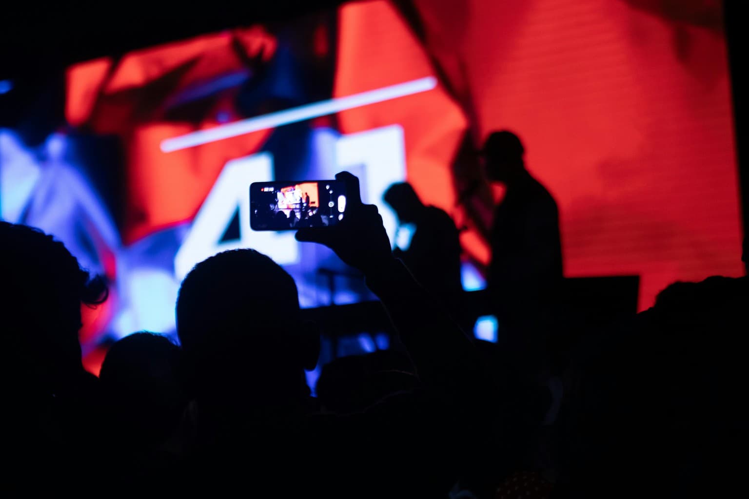 Public la un concert filmând cu telefonul un ecran LED roșu